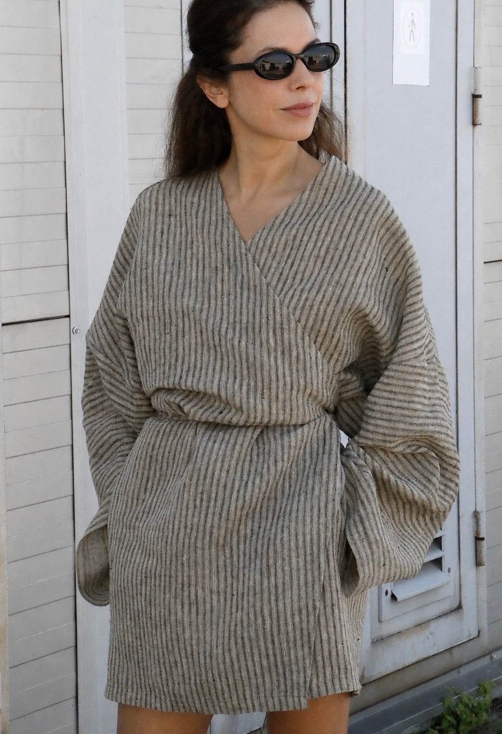 Woman wearing a natural linen kimono mini dress with wrap waist, oversized sleeves and hidden pockets.