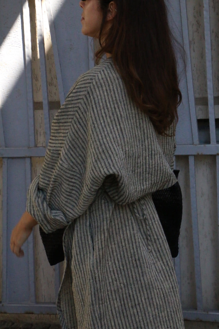 Woman wearing a striped linen kimono wrap dress with oversized sleeves and an adjustable waist tie.